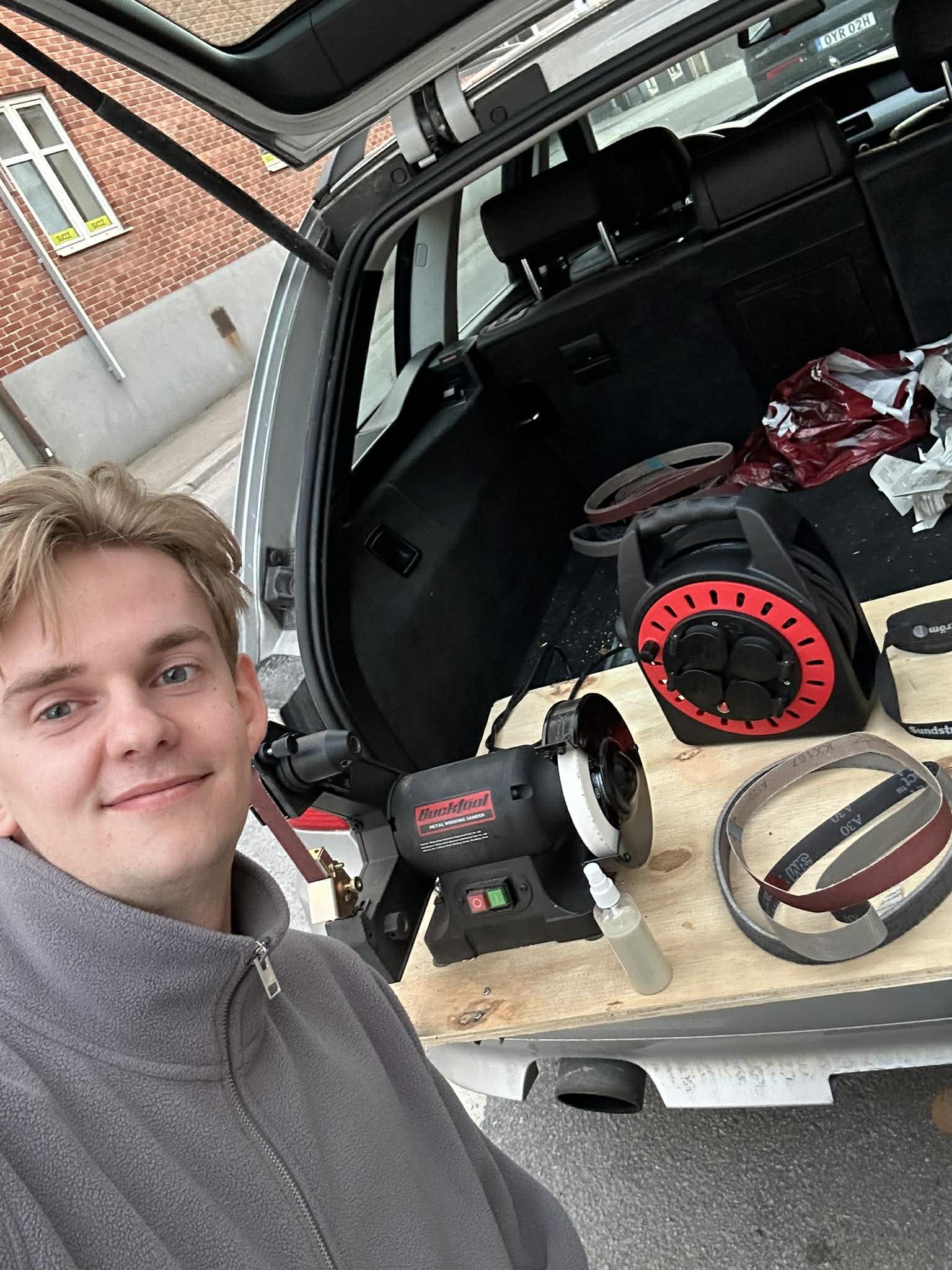 Malte Ljungström vid bakluckan på slipbilen — andningsskydd och slipmaskin synliga