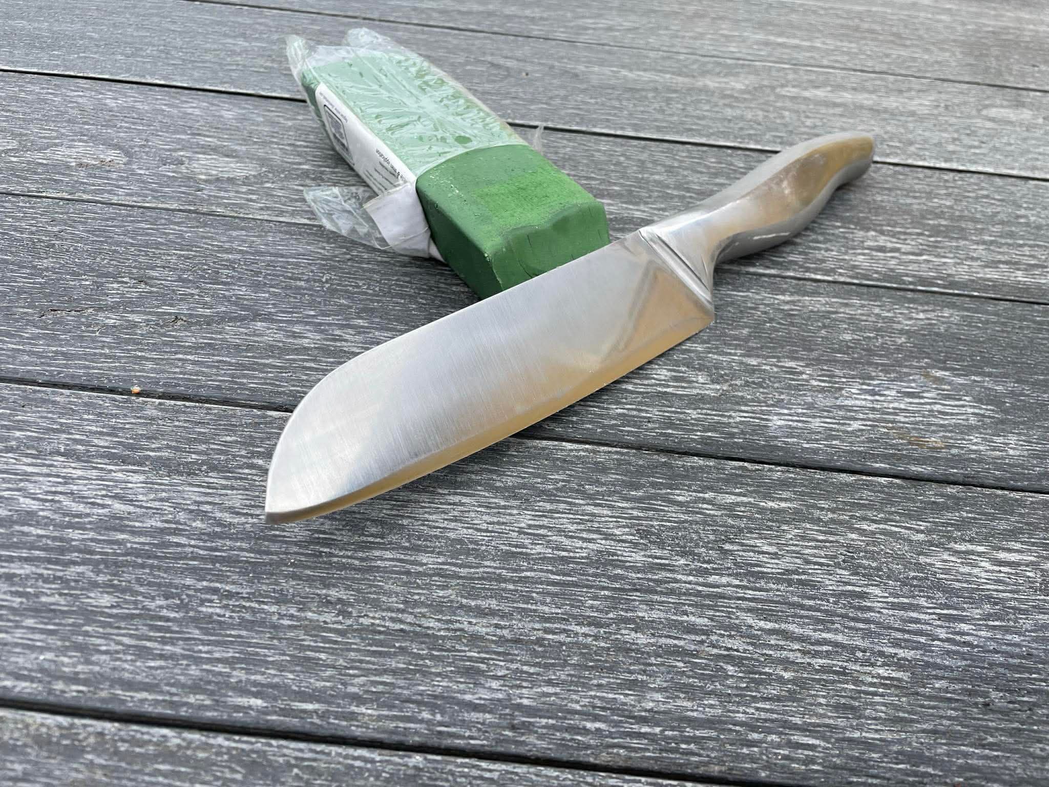 Santoku-kniv med grönt vaxpapper på handtaget på grått trädäck